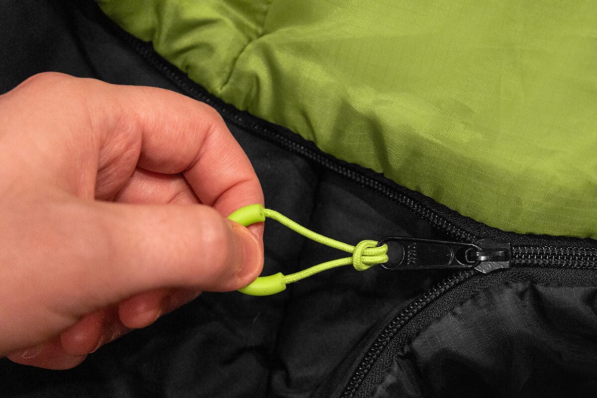 A person holding onto the zipper of their sleeping bag.