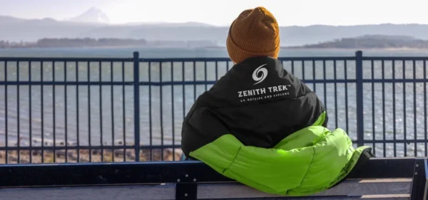 A person sitting on top of a bench near the water.